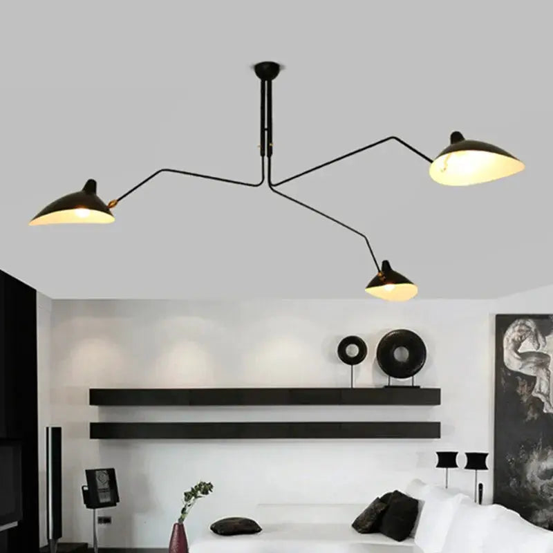 Spider pendant light with three black metal arms and warm lamps over a modern living room.