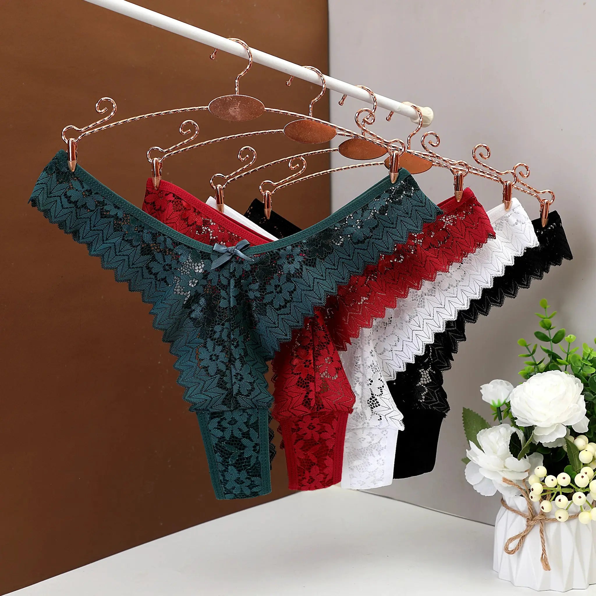 Five lace panties on copper hangers in teal, red, green, white, and black, with floral lace patterns.
