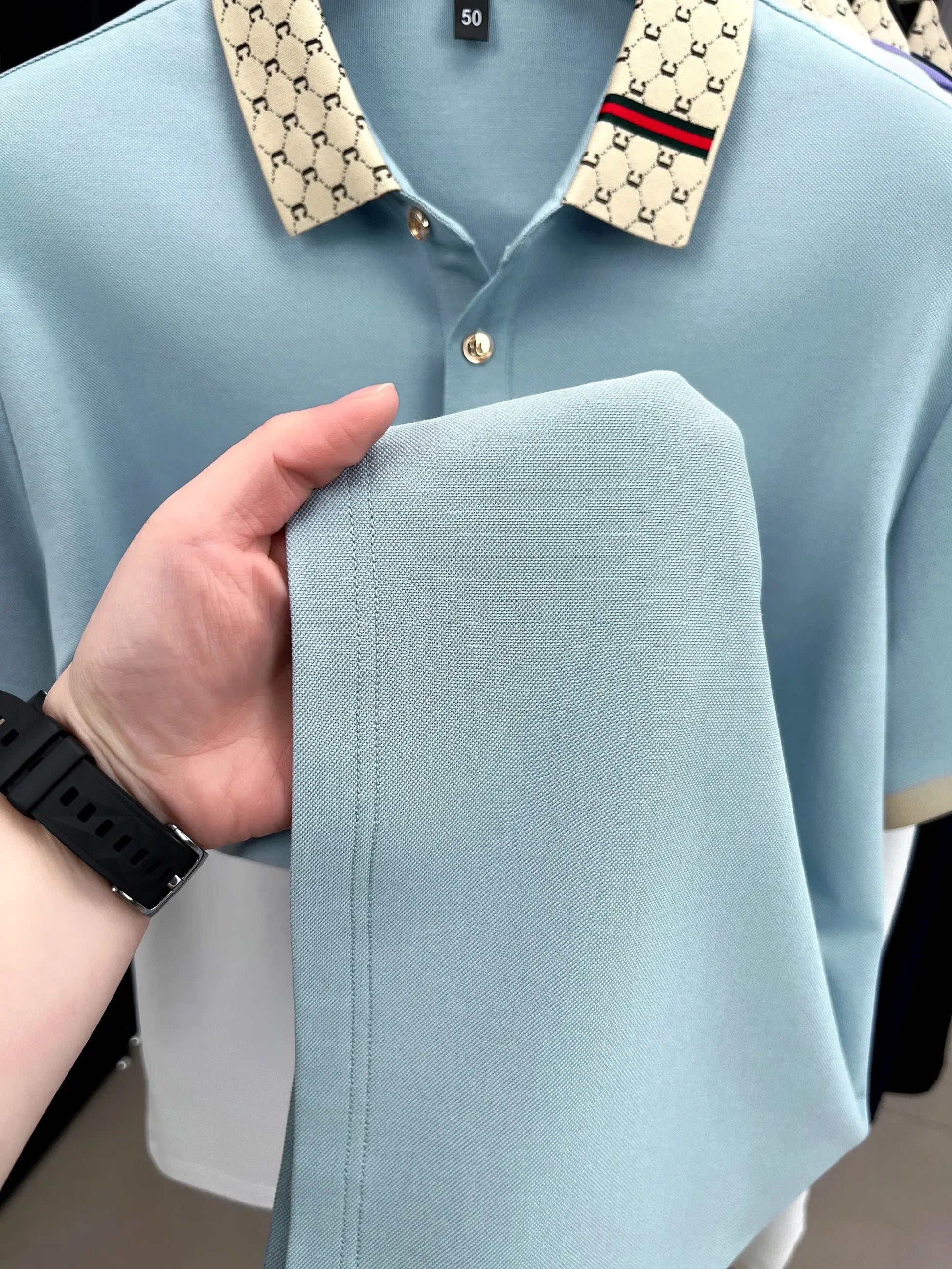 Light blue men's polo with cream patterned collar and red-green stripe; single button placket.