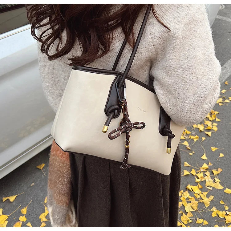 PU leather shoulder bag for women, beige with black trim, crossbody with brown bow charm and gold hardware
