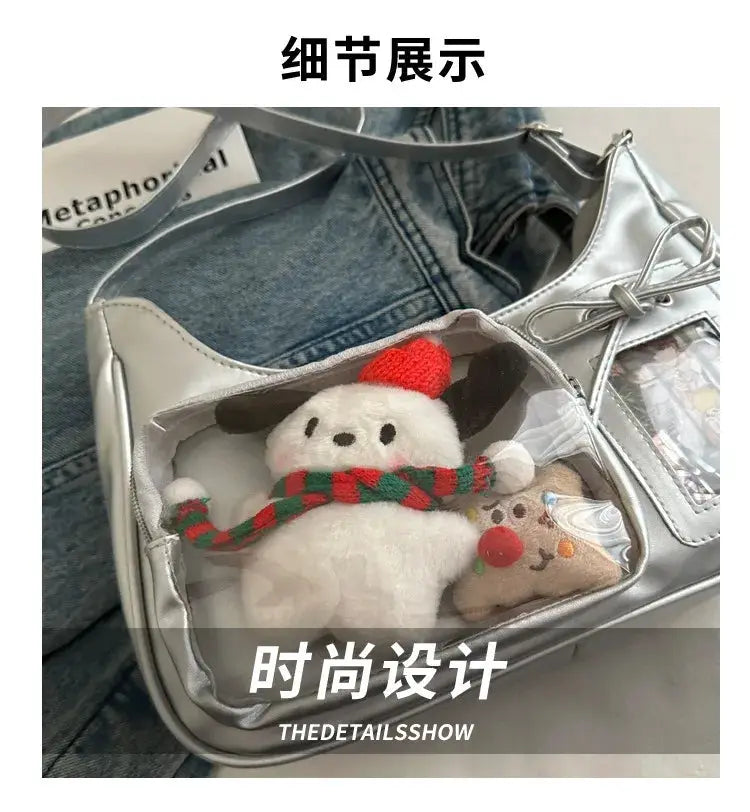 Silver transparent Ita bag with a clear front pocket; two plush figures (snowman in red hat and reindeer) inside.