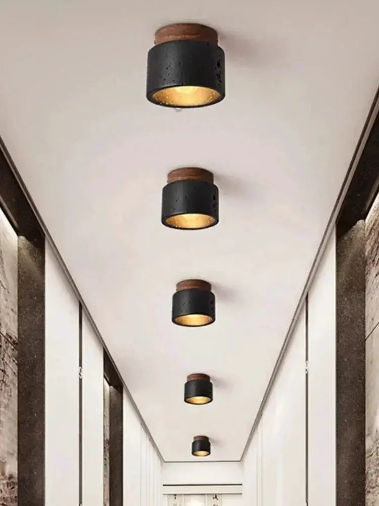Wabi-sabi ceiling lamp black cylindrical fixtures with wood accents along a hallway; five lights emit warm amber glow.