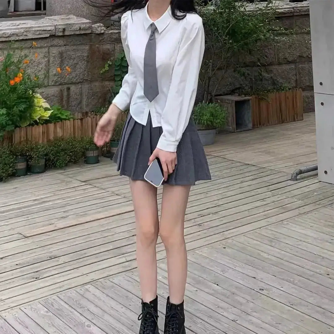 Women's white button-down shirt with gray tie, paired with a gray pleated mini skirt and black ankle boots