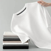 Men's white waffle-knit short-sleeve T-shirt with round neck draped over a stack of folded tees in neutral colors