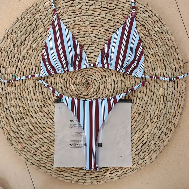 Striped micro bikini set with triangle top and thong bottom on a woven mat; blue, burgundy and white stripes.