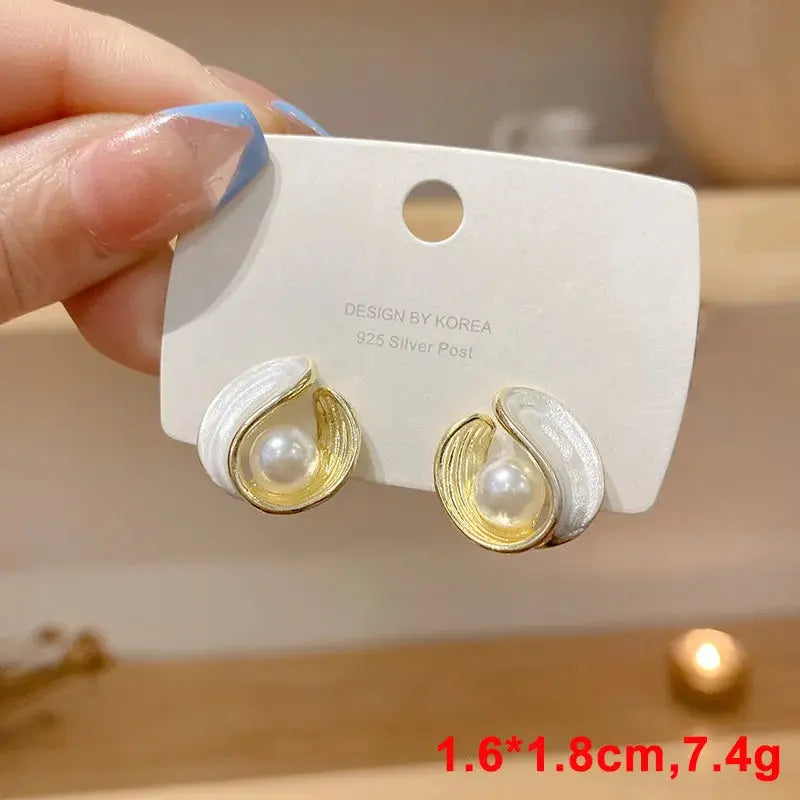 White dangle earrings by Simples Market with gold-toned swirl, pearl centerpiece and acrylic enamel detailing
