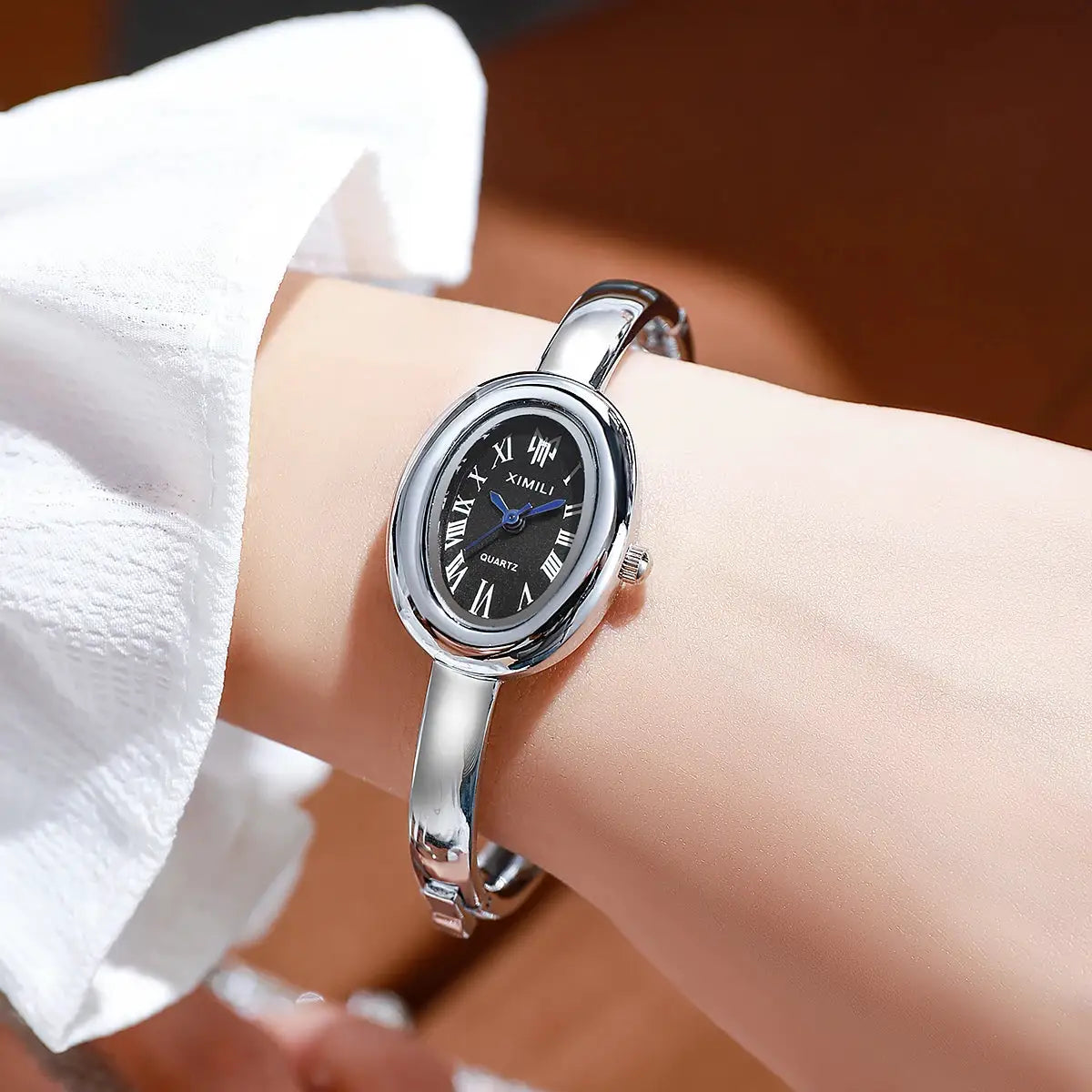 XIMILI quartz women's wristwatch with a silver stainless-steel bracelet, black Roman numeral dial, blue hands