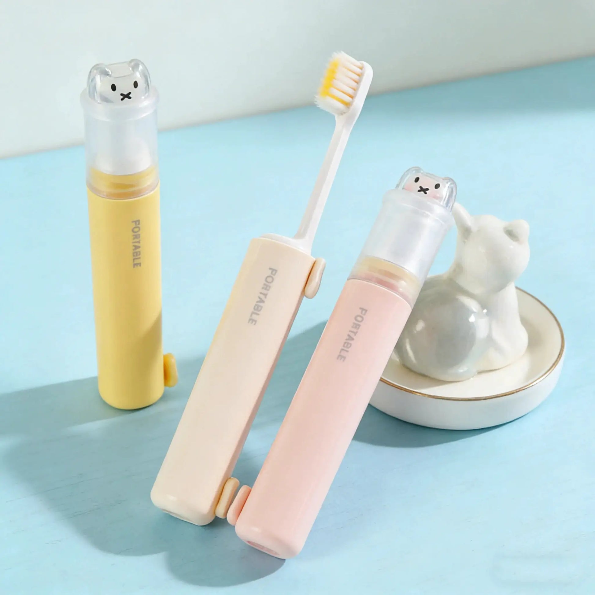 Three pastel 2-in-1 foldable travel toothbrushes with bear-dust covers in macaron colors by Simples Market.