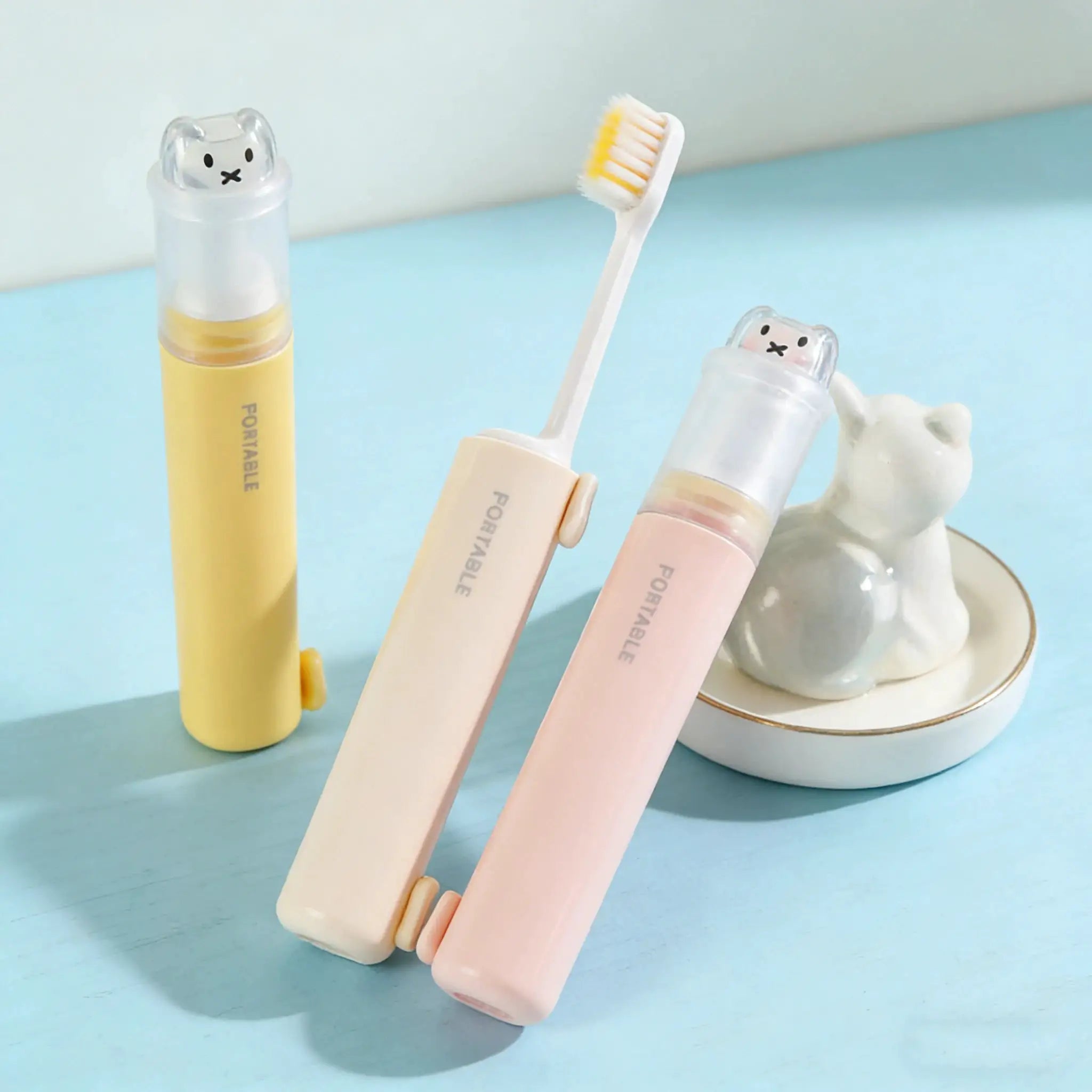 Three pastel 2-in-1 foldable travel toothbrushes with bear-dust covers in macaron colors by Simples Market.