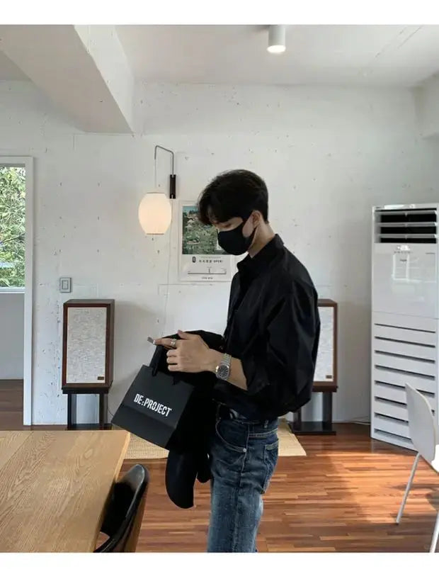 Men's black slim-fit cardigan-style shirt, solid color long sleeves; model indoors with a DE:PROJECT bag.