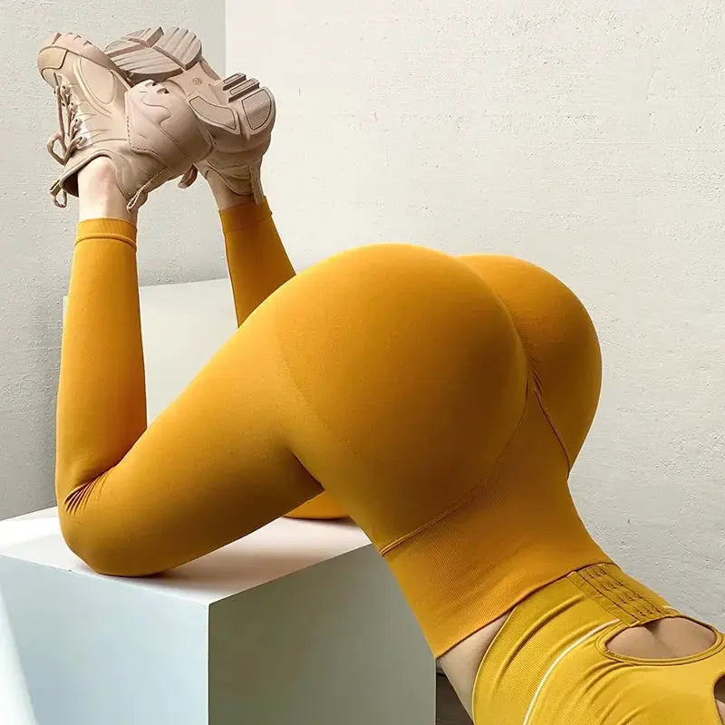 Seamless knitted women's leggings in mustard yellow with high-waist fit, shown on a model in athletic sneakers.
