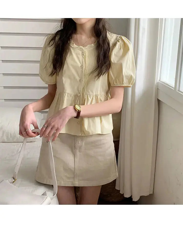 Women's pale-yellow puff-sleeve blouse with button front and peplum waist, paired with beige mini skirt and white bag.