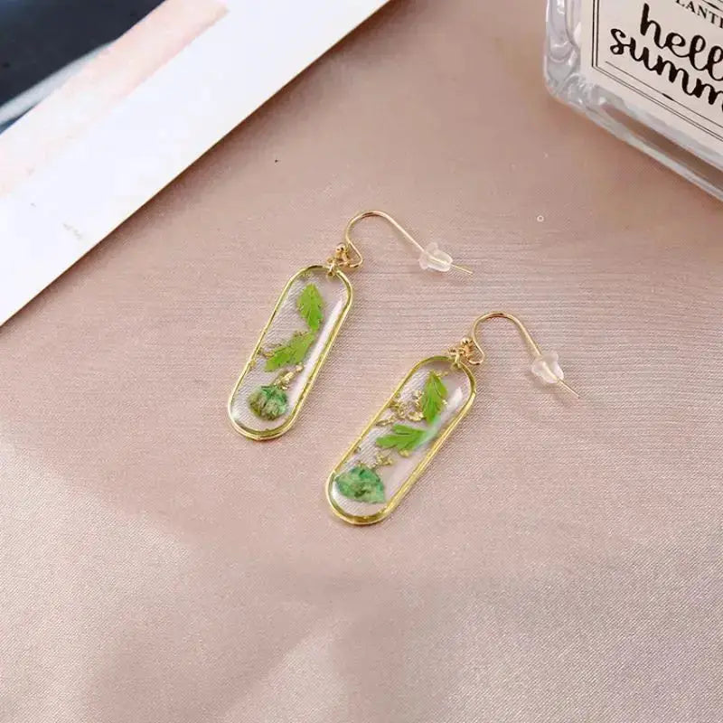 Geometric pressed-flower epoxy resin earrings with gold-tone rectangular frames and green leaves, a pair