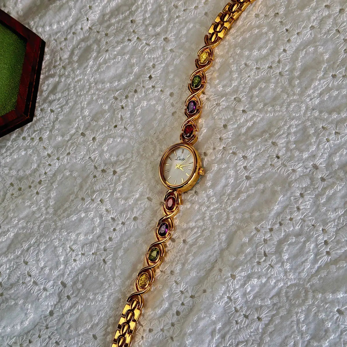Women's gold-tone bracelet watch with colorful tourmaline stones and an oval mother-of-pearl dial.