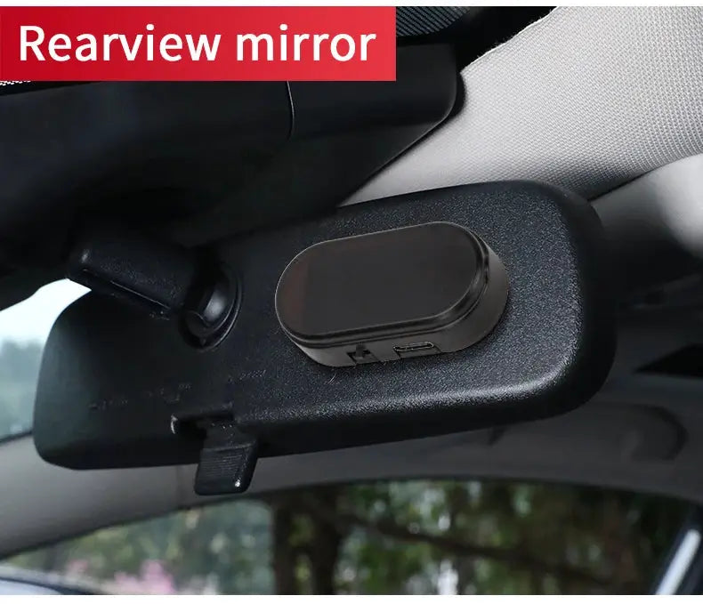 Solar-powered car security light, black oval unit attached to rearview mirror; simulated wireless alarm signal