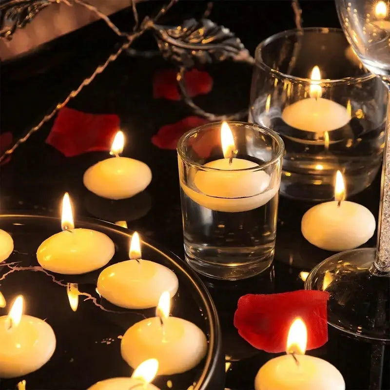 Floating white disc candles; unscented, several lit on a black reflective surface with rose petals and glass holders.