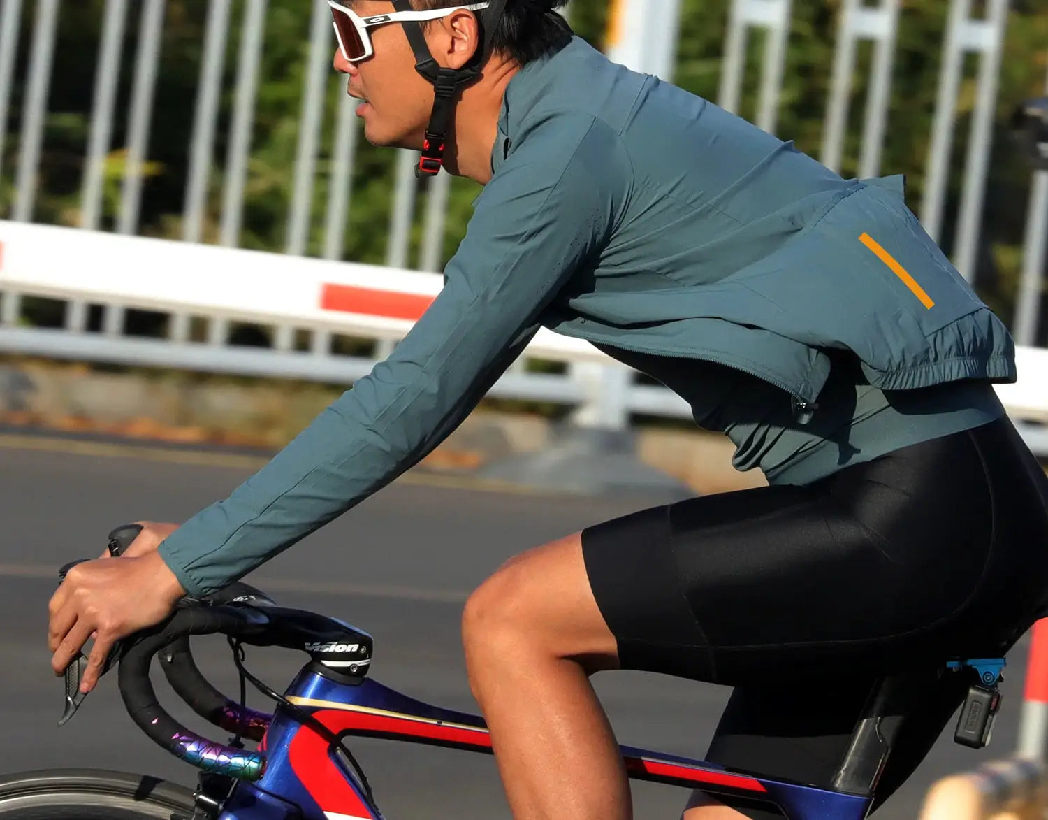 SPEXCEL 2022 lightweight windproof cycling jacket in teal with 3 back pockets, worn by cyclist.