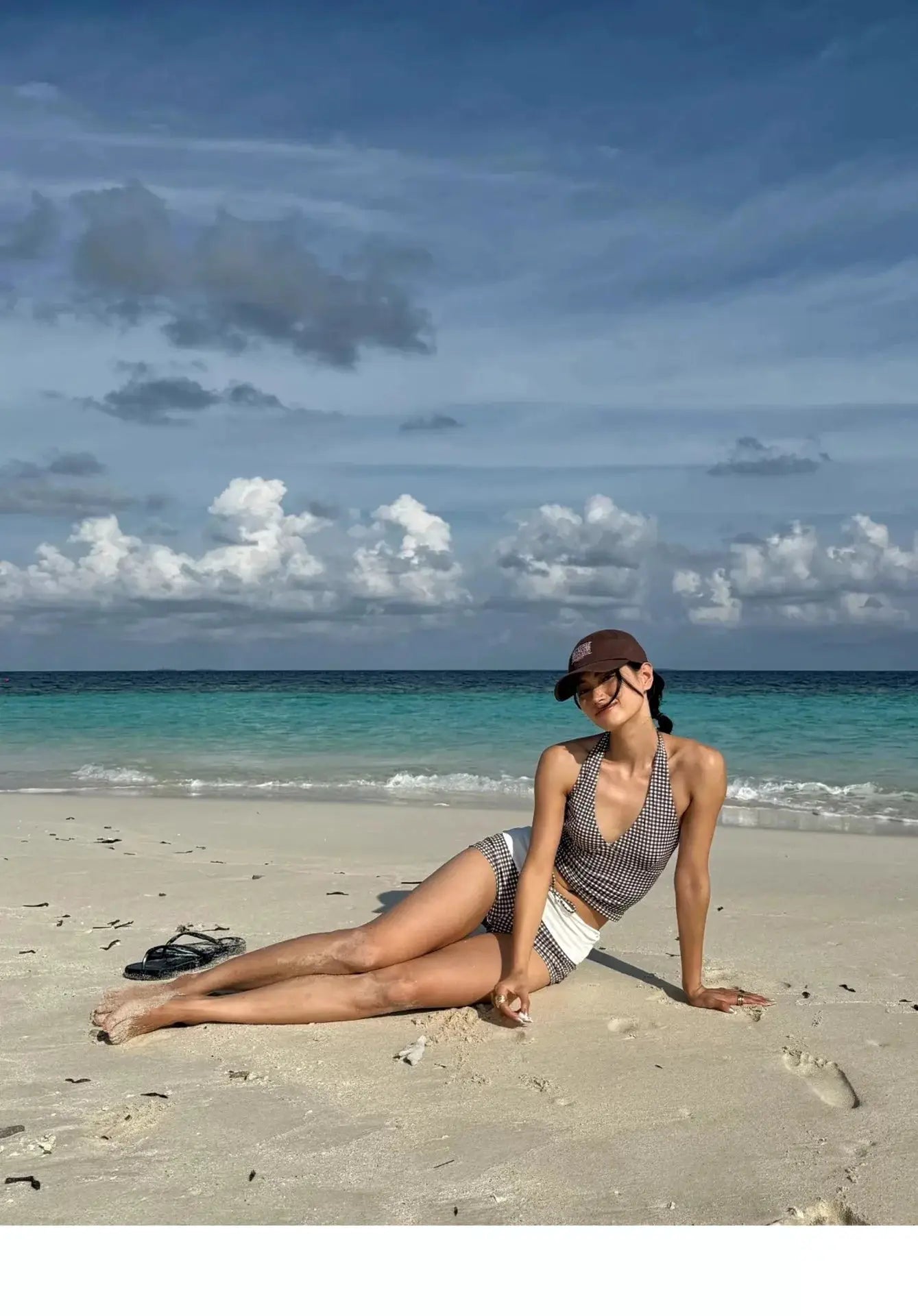 Two-piece bikini set on a beach model; black-and-white checkered, high-waisted bottom with deep V push-up top.