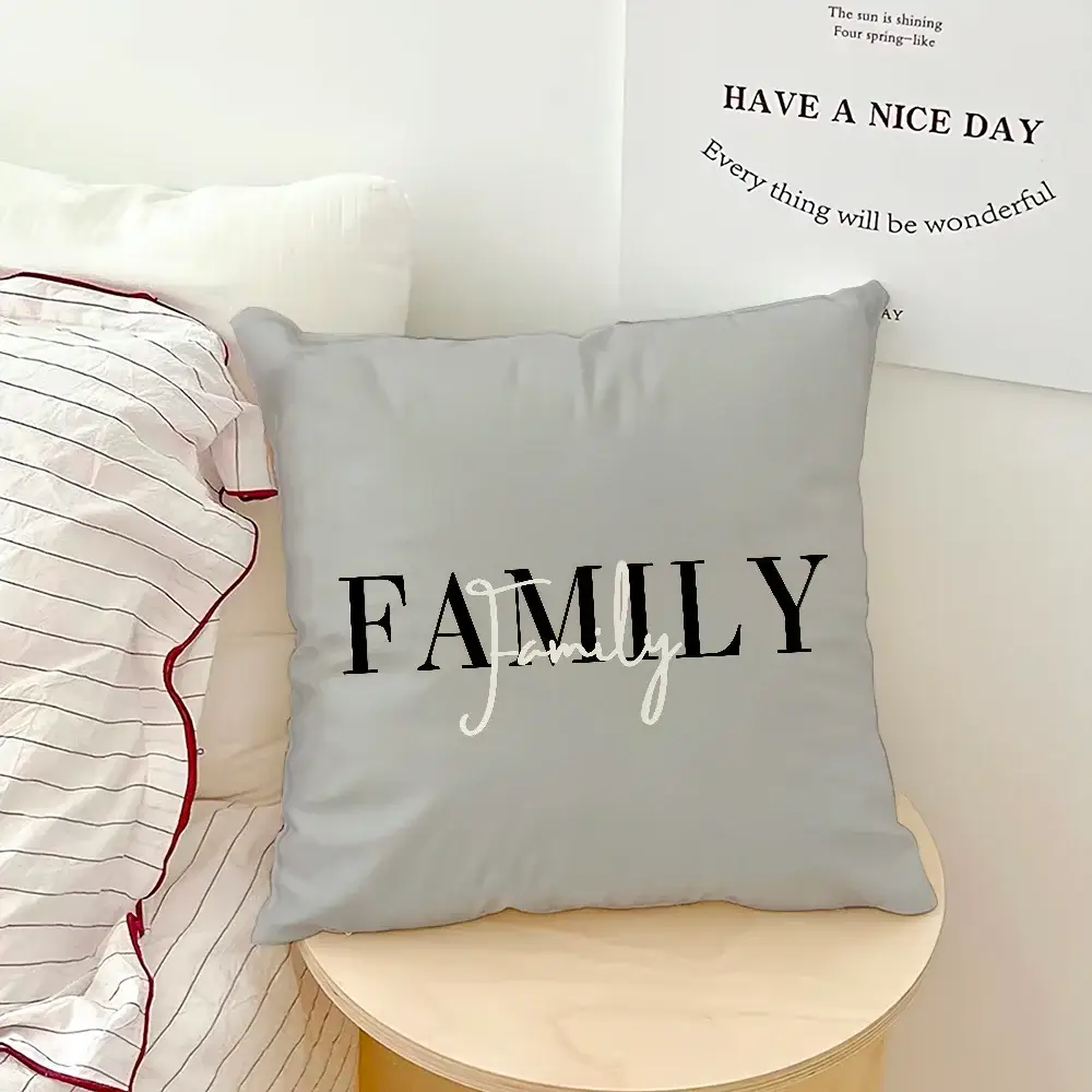Gray decorative throw pillow with large FAMILY black letters and white cursive overlay on light wood table
