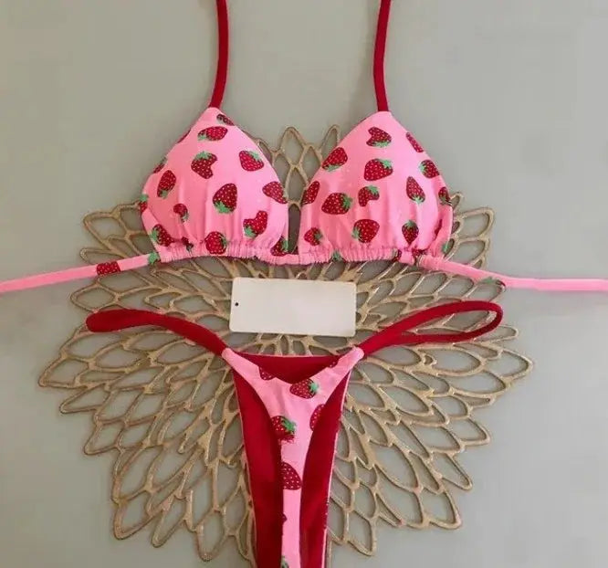 Pink strawberry-print bikini set with halter top and thong bottom, red straps.