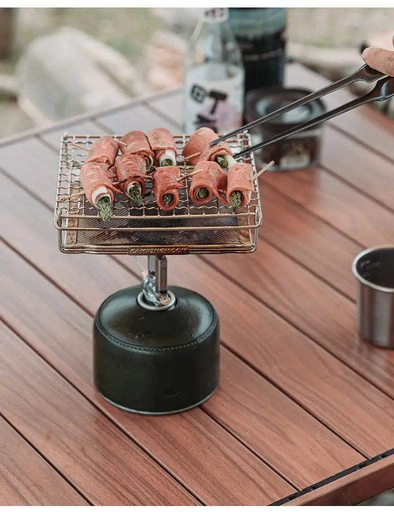 CAMPINGMOON stainless steel folding grill net on a portable gas stove with several pink meat rolls