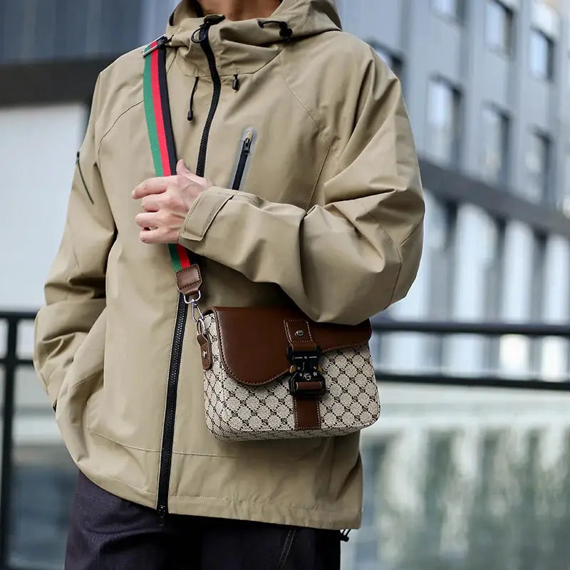 Men's crossbody bag by Simples Market; beige jacquard pattern with brown leather flap and green-red strap.
