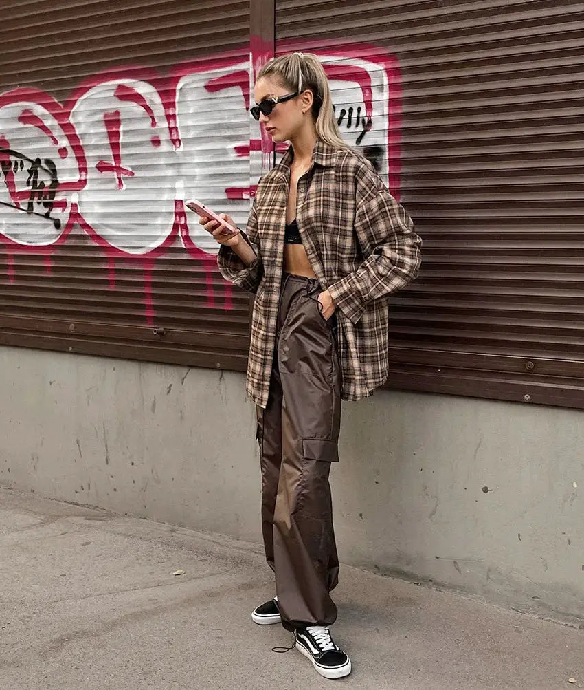 Women's oversized brown plaid shirt worn open over a black crop top, paired with brown cargo pants and sneakers