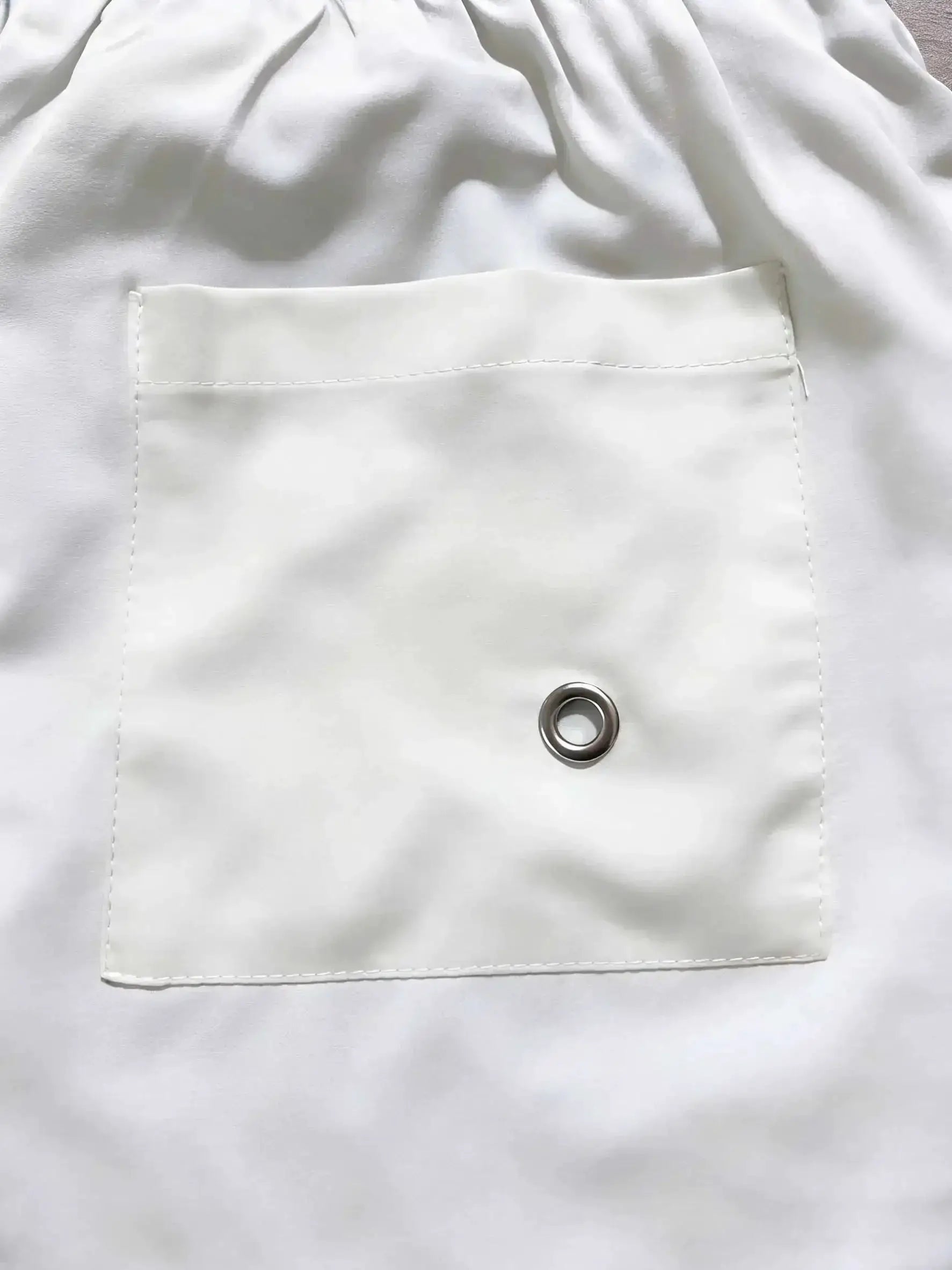 Men's white swim trunks with elastic waist, front pocket and metal grommet detail