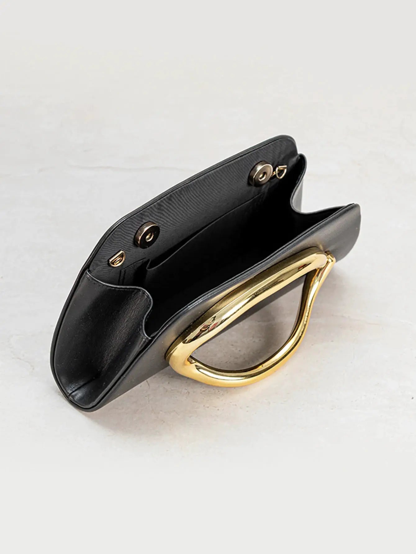 Box clutch in black with gold-tone metal buckle and curved handle; evening bag