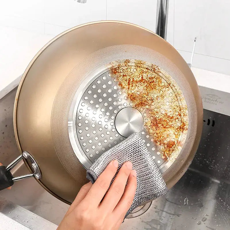 Steel wire cleaning cloth scrubbing a burnt nonstick pan with brown residue