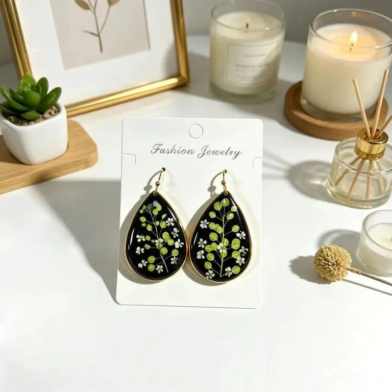 Pair of teardrop pressed-flower earrings in black with gold edging; green leaves and white blossoms, Simples Market