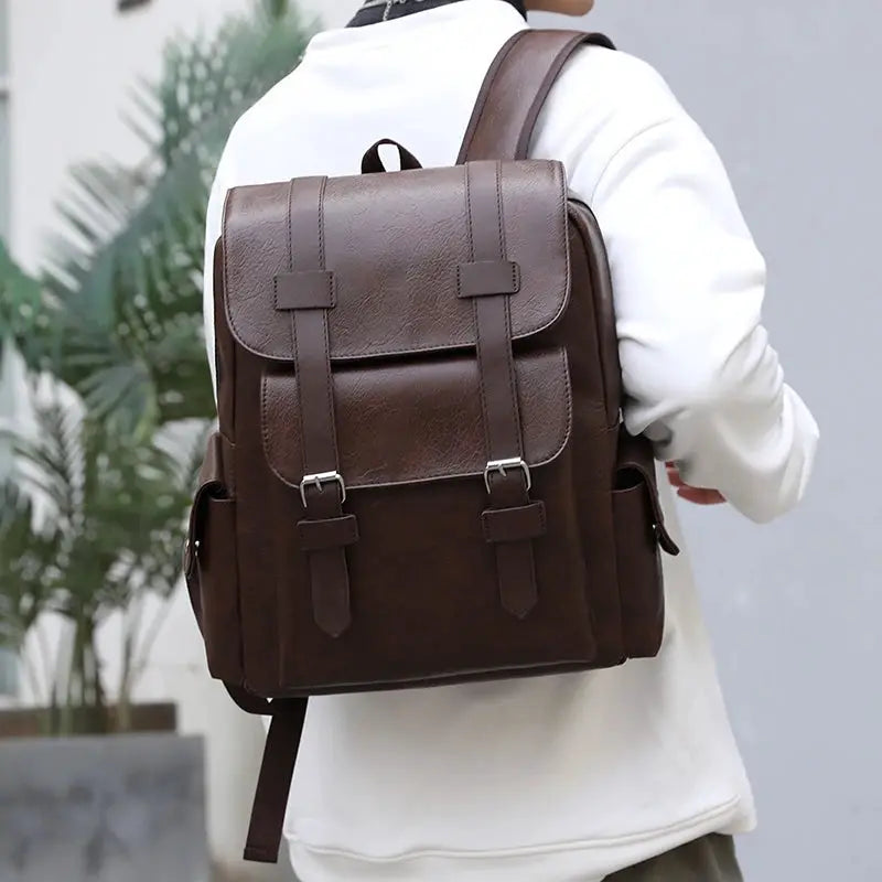 Brown PU leather backpack with buckle straps, large laptop backpack worn by a person in a white hoodie