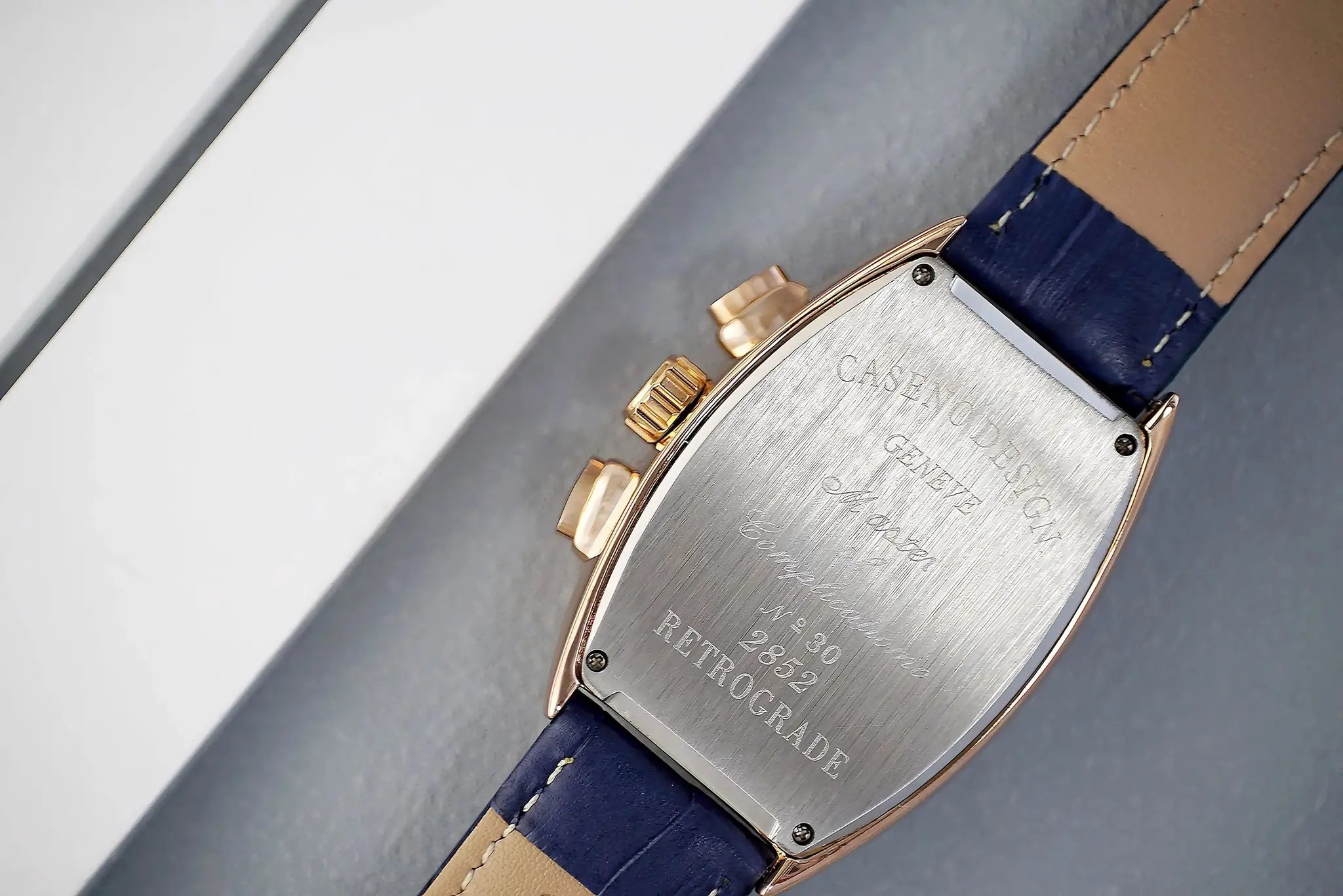 Men's rose-gold tonneau luxury watch back, engraved case plate, crown and pushers, blue leather strap