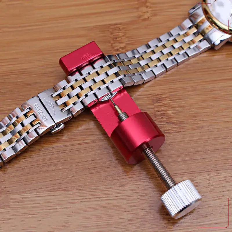 Watch link pin remover tool with red anodized body clamping a two-tone stainless steel bracelet