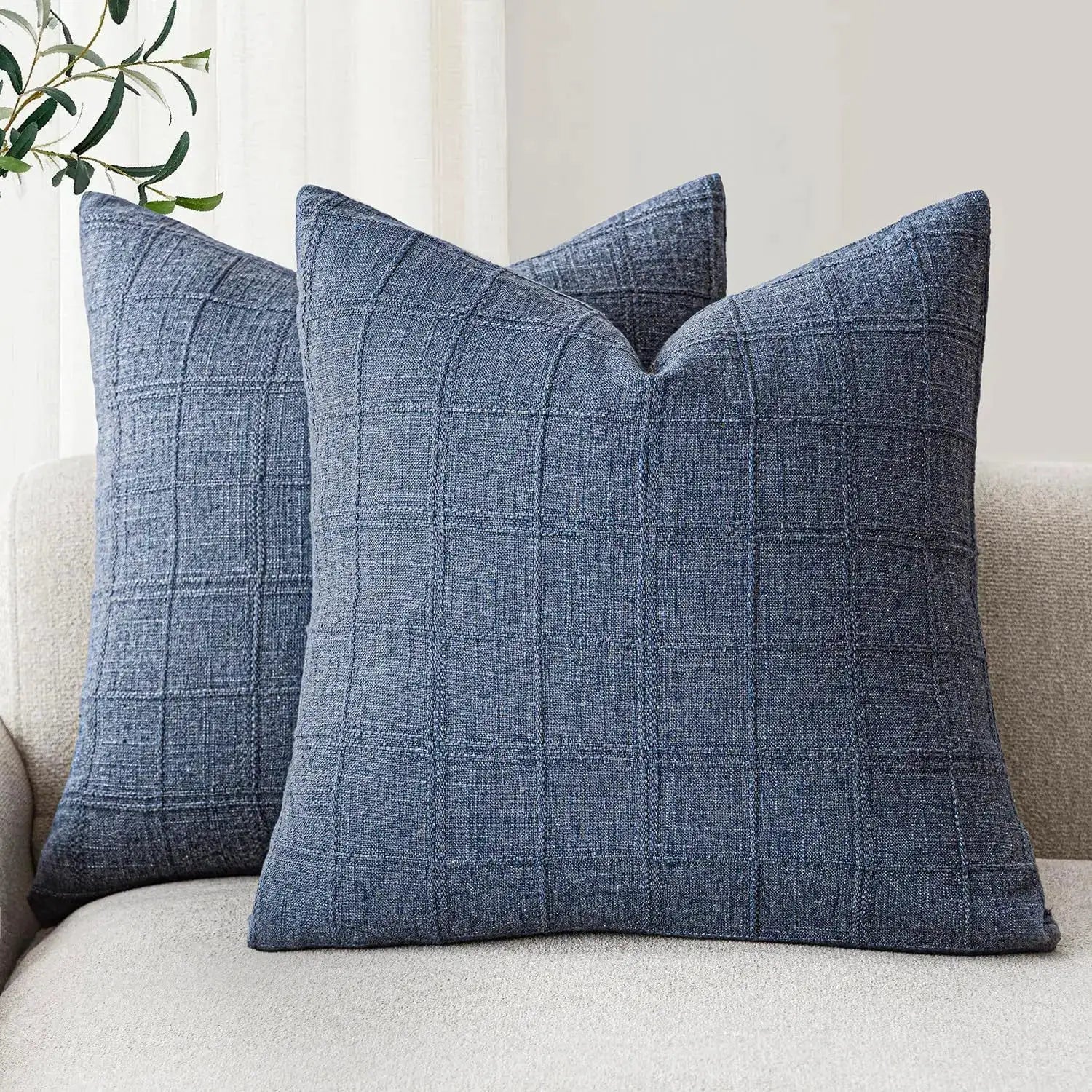 Two blue square cushion covers with a denim grid pattern on a beige sofa.