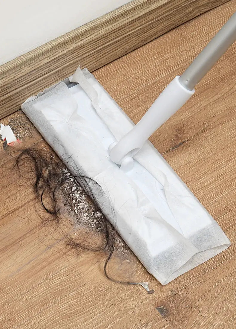 Disposable dust-removal mop pad attached to a flat mop head, white paper pad with debris on wood floor