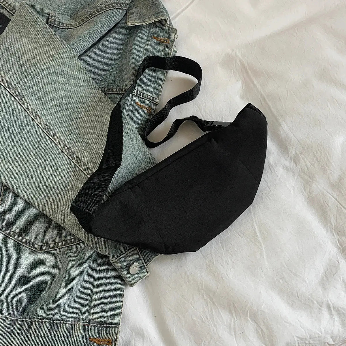 Fanny pack black fabric with adjustable strap beside a denim jacket