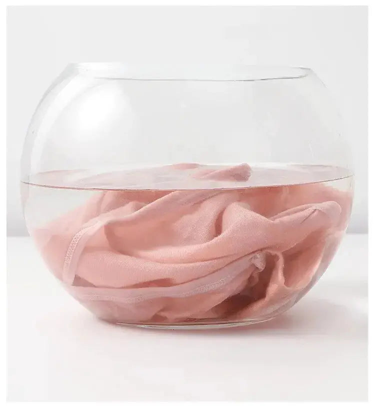 Cotton panties, pink, submerged in water inside a clear glass bowl.