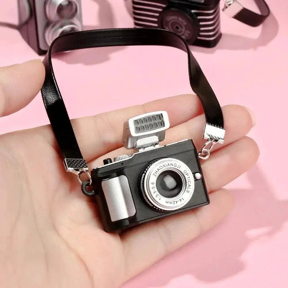 Dollhouse miniature digital SLR camera with black body, silver lens ring and strap