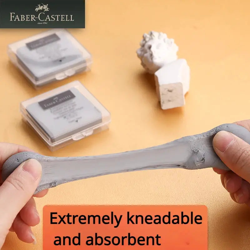 Faber-Castell kneaded eraser, gray, stretched by hands; two plastic eraser boxes visible in background