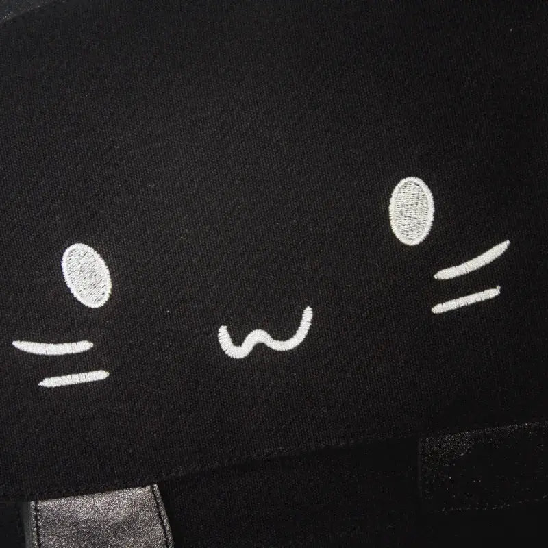 Backpack in black with a white embroidered cat-face design; large-capacity, cute cartoon style.