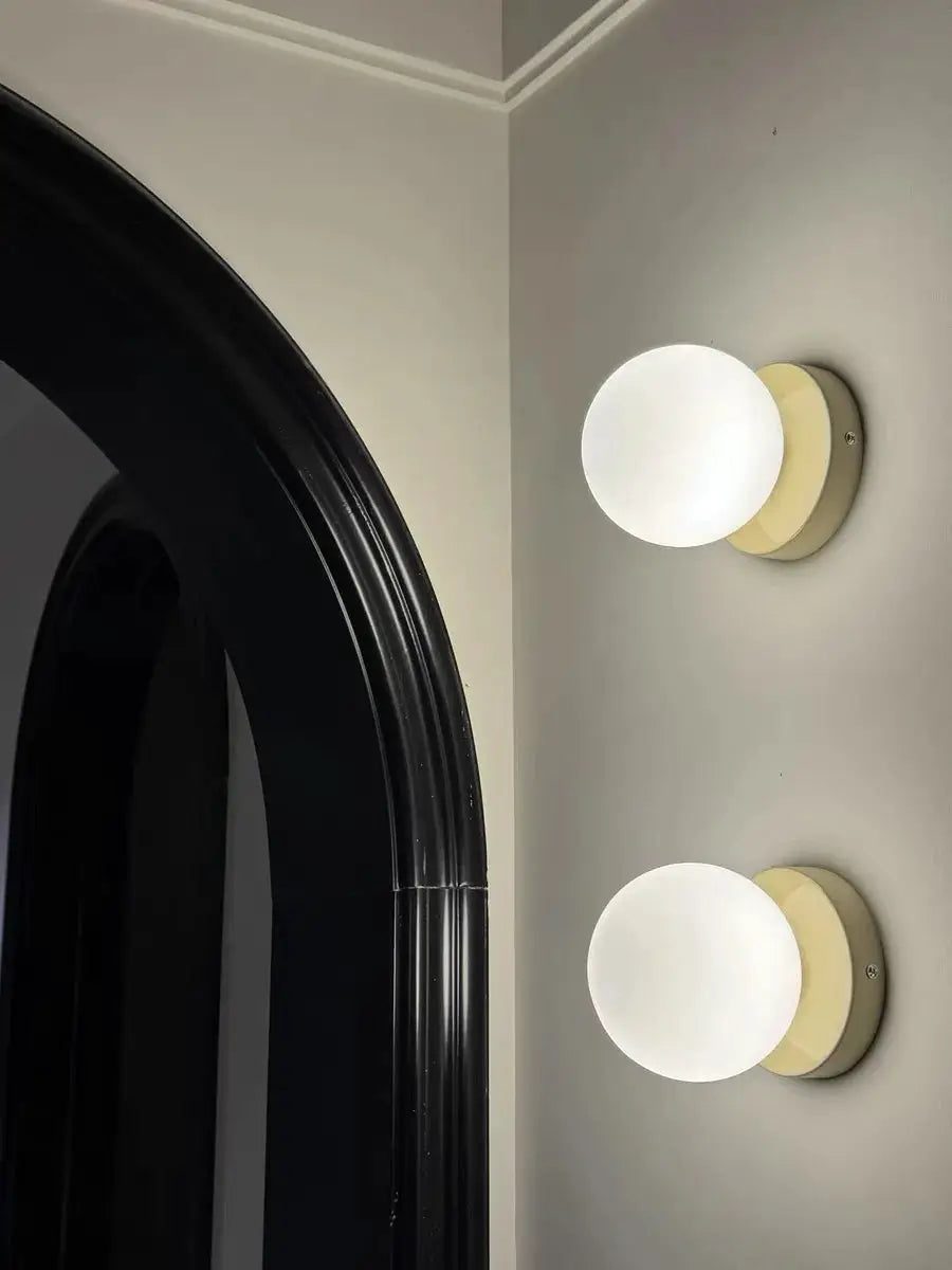 Two macaron-style wall lamps with iron bases and frosted white ball shades on beige mounts.