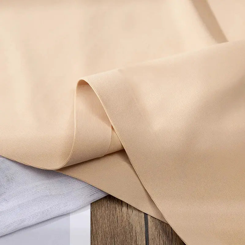 Ice silk fabric swatch in beige, folded edge on wood surface