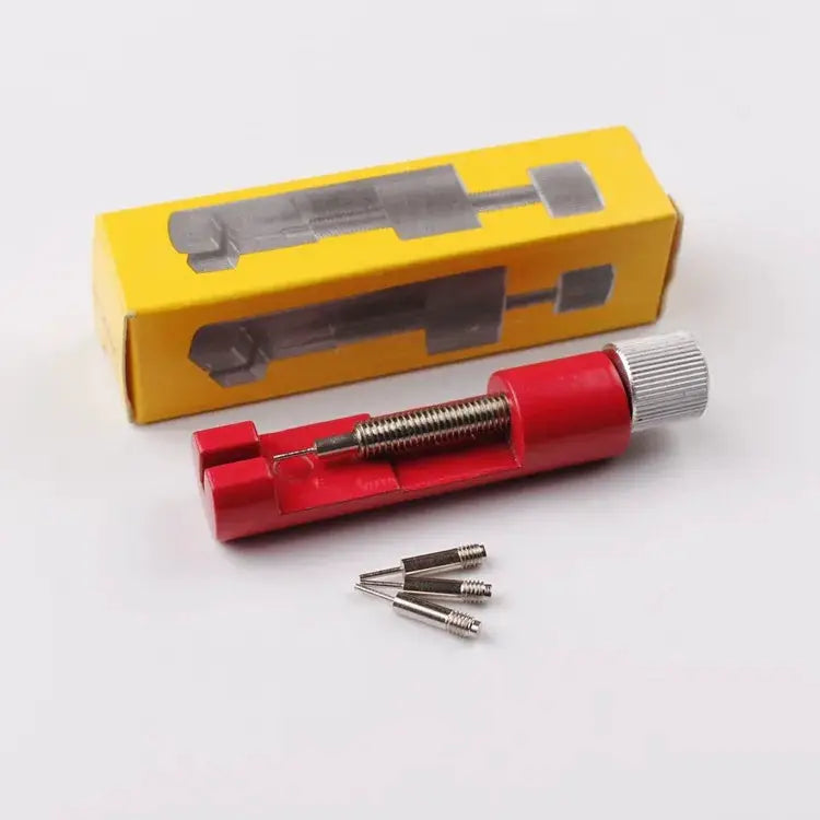 Red metal watch strap link pin remover tool with screw, three spare pins, beside yellow packaging box