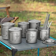 Tiartisan titanium camping cookware set with folding handles; cups, pots and lids on a camping table