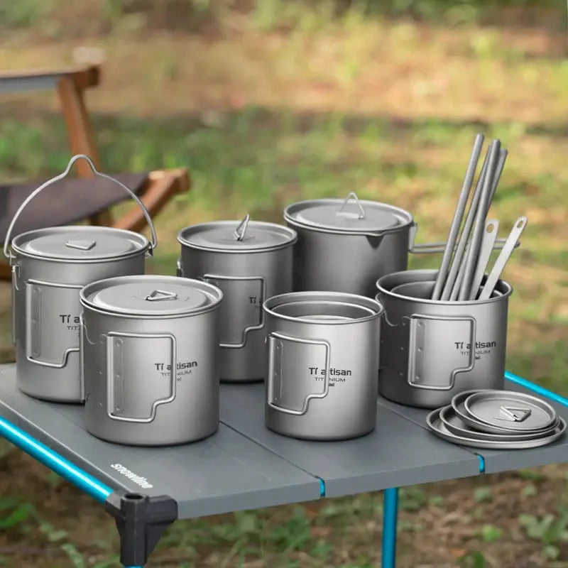 Tiartisan titanium camping cookware set with folding handles; cups, pots and lids on a camping table