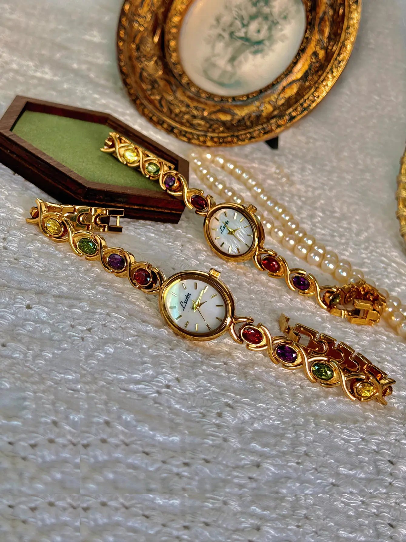 Two gold-tone luxury women's watches with colorful gemstone link bracelets and oval mother-of-pearl dials