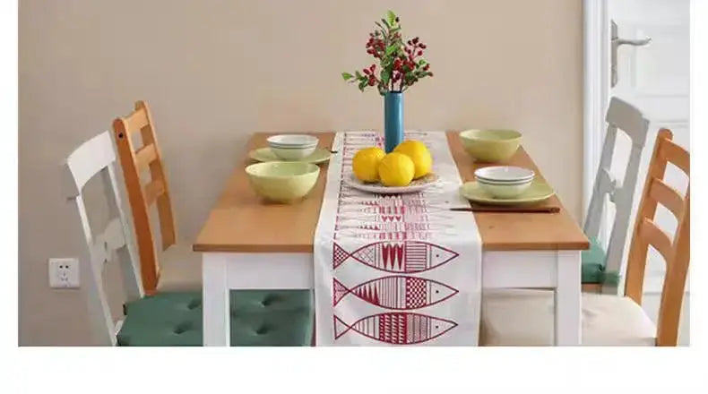 Dining table setting with fish-pattern table runner, blue vase of red flowers, lemon centerpiece, and green bowls.