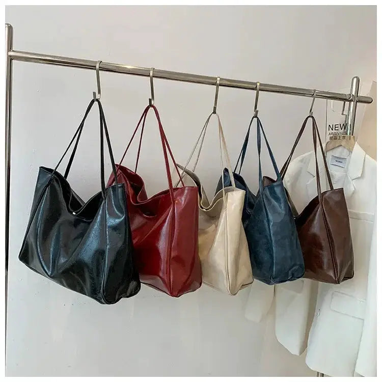 Six women's tote bags in black, red, beige, cream, blue, and brown PU leather, hanging on a rack.