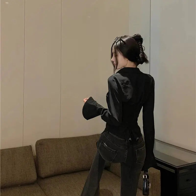 Women's black wrap blouse with long bell sleeves and back tie, paired with dark jeans